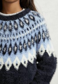 Kék és fekete mintázatú pulóver bolyhos textúrával, világoskék, fehér és fekete díszítésekkel ellátott geometriai mintával.