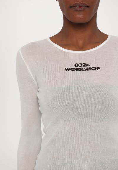 Fehér, hosszú ujjú, bordázott felső kerek nyakkal. A mellet díszíti a "032c WORKSHOP" felirat vastag fekete betűkkel. Fél áttetsző anyag.