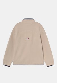 Beige fleece pullover met een hoge kraag. Bevat een geborduurd "TOMMY HILFIGER" logo en een klein vlagaccent in blauw en rood in het midden.