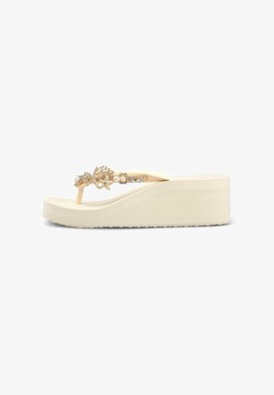 Sandalia beige de cuña con tiras decoradas en tono dorado con perlas y pedrería, mostrada en perfil lateral sobre fondo blanco.