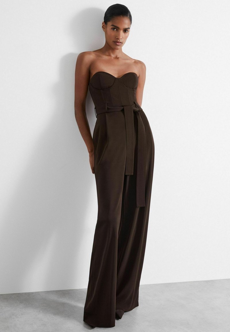 Helfri brun jumpsuit med en åtsittande bodice, vida ben och ett knytbälte i midjan. Slät tyg och strukturerad design.