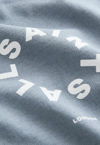 Tissu bleu clair avec des lettres blanches en gras disposées en cercle et le mot « LONDON » imprimé en dessous du texte.