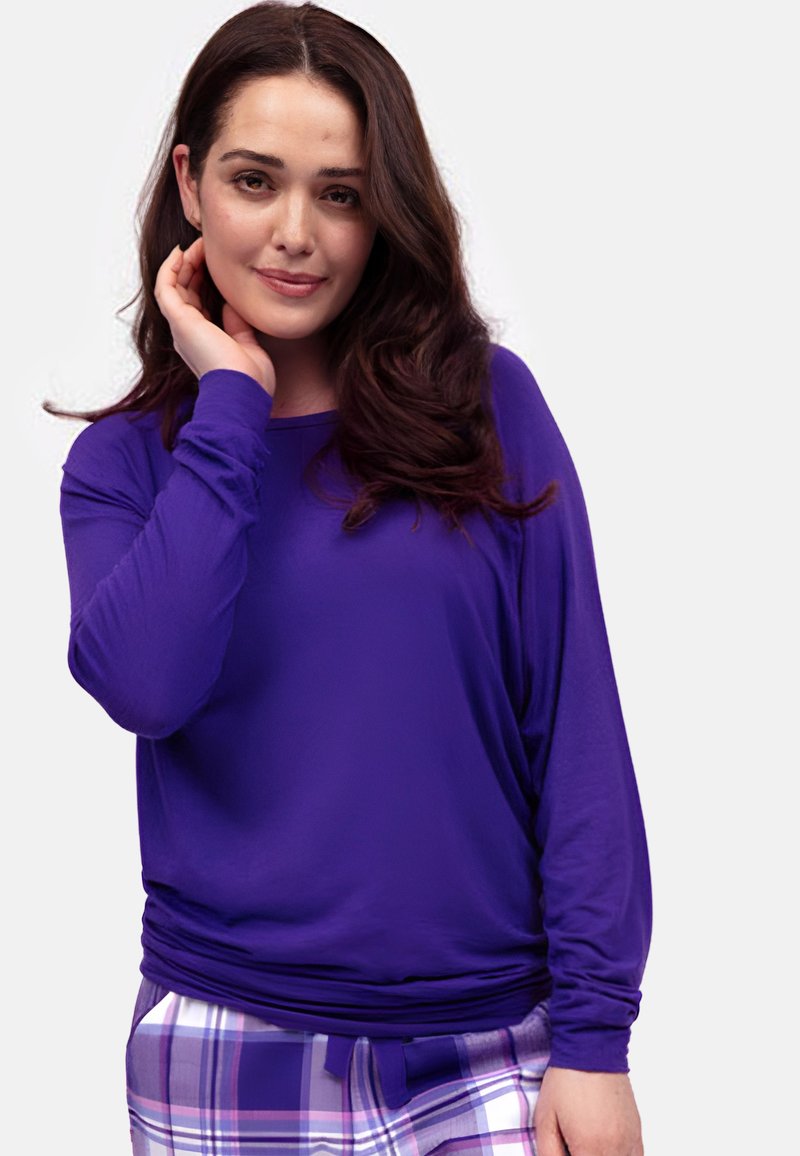 Fioletowa bluzka z długim rękawem, wykonana z lekkiego materiału, o luźnym kroju i marszczonym pasie; zestawiona z spodniami w kratę w delikatnych kolorach.