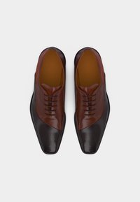 Ζευγάρι από γυαλισμένα καφέ δερμάτινα παπούτσια με μαύρες μύτες και κορδόνια, φωτογραφημένα από ψηλά σε λευκό φόντο.