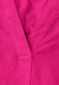 Gros plan sur un tissu rose vif montrant une couture en V et des points de couture détaillés avec une texture semblable à du lin.