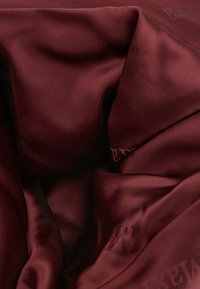 Tissu rouge profond lisse avec des plis doux et des ombres subtiles, montrant un texte partiellement embossé ou imprimé en surface.