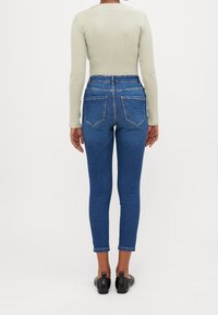 Jeans ajustados en denim de lavado medio con una cintura alta y diseño de cinco bolsillos, combinados con una camiseta de manga larga ajustada de color verde claro.