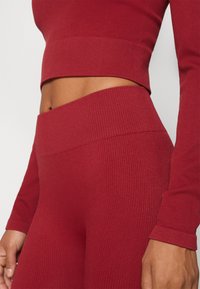 Rebrasti crveni crop top i visoko strukirane tajice, s teksturiranim materijalom, prilagođenim dizajnom i bešavnom pojasom.