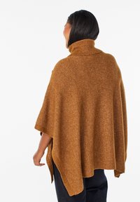 Brązowy dzianinowy poncho z prążkowanym golfem, charakteryzujące się luźnym krojem i bocznymi rozcięciami dla swobody ruchów. Teksturalna tkanina dodaje wymiaru.