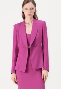 Blazer fuchsia au design structuré avec deux boutons, revers crantés et coupe cintrée. Assorti à un haut ajusté. Texture lisse.