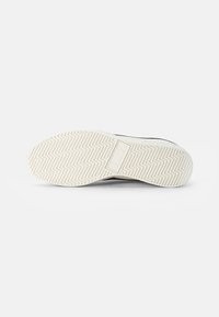 White rubber sneaker sole with a zigzag tread pattern and a subtle logo detail at the center. Smooth, flexible material.