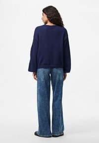 Navy blue knit sweater with dropped shoulders, paired with high-waisted, wide-leg, faded denim jeans. Visible stitching on sweater hem.
