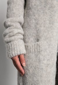 Jasnoszary sweter warkoczowy z teksturowanej wełnianej mieszanki, szerokimi ściągaczami i luźnym krojem oraz boczną kieszenią.