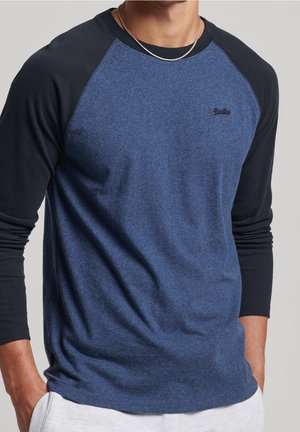 Chemise à manches longues avec un corps bleu et des manches raglan noires. Tissu doux avec une légère texture chinée et un détail subtil de logo sur la poitrine.