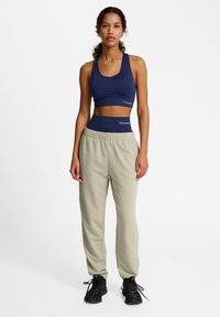 Marinblå sportbehå med racerback-design, kombinerad med ljusgröna träningsbyxor med elastisk midja, iförd med svarta träningsskor.