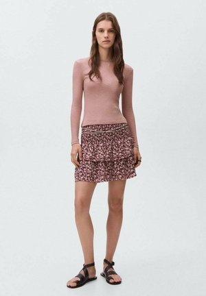 Pitkähihaisen vaaleanpunaisen istuvan paidan parina on rypytetty, polvipituinen hame, jossa on tumma kukkakuosi. Mustat olkaimelliset sandaalit viimeistelevät ilmeen.