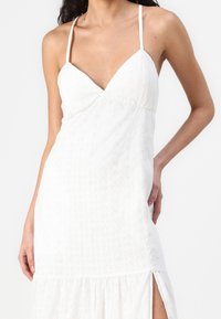 Vestido blanco de algodón con escote en V, tirantes delgados, tela texturizada y abertura lateral en el dobladillo. Detalles de bordado floral en todo el vestido.