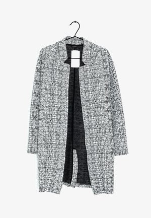 Zwart-wit gestreepte open voorjak, voorzien van een kraag, geometrische ontwerpen en een textielachtige stof. Hangt aan een zwarte haak.