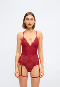 Rød blonde bodysuit med justerbare stropper, dyp V-hals, blomsterdesign, gjennomsiktig nedre panel og festede strømpeholdere.