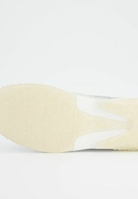 Vit sneakersula med en texturerad gummiyta med ett vågmönster. Midsulan har en krämfärg som kontrasterar med ovandelen.