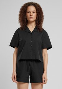 Maglietta nera a maniche corte con colletto e chiusura a bottoni, abbinata a pantaloni corti neri coordinati. Entrambi presentano una finitura in tessuto con texture.