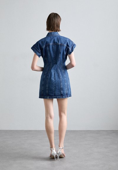 Rochie din denim cu mâneci scurte răsucite, talie ajustată și un tiv scurt; prezintă cusături vizibile și guler, asortată cu tocuri argintii.