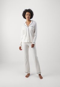 Vitt pyjamaset med svart piping. Överdelen har en knappstängning och bröstficka; byxorna är raka och i en texturerad tyg.