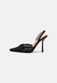 Tacones negros de encaje con tira en el talón, punta afilada, tacón delgado negro y detalle de lazo en la parte delantera. Capa de encaje texturizado con suela suave.