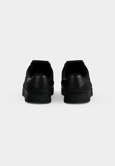 Ζευγάρι μαύρα παπούτσια τύπου low-top, φαίνονται από πίσω σε απλό ανοιχτό γκρι φόντο.