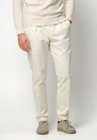 Weiße Baumwollhose mit Falten und einem lockeren Schnitt, kombiniert mit hellbeigen Sneakers. Das Material hat eine glatte, weiche Textur.