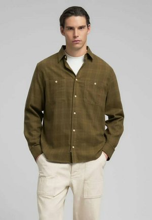 Chemise à carreaux vert olive en tissu doux, dotée de deux poches poitrine et de boutons blancs, associée à un pantalon cargo beige clair.