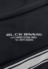 Zwart fabric met een textuurweefsel, met geborduurde logo's in contrasterend wit. Bevat twee horizontale witte strepen langs de rand.