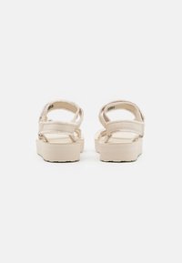 Beige platform sandals featuring adjustable straps, textured fabric, and a sturdy outsole. The design is minimalistic with a flat sole.