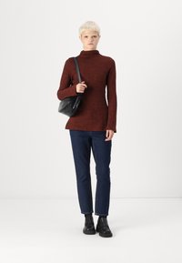 Pulover cu guler înalt de culoare ruginie, cu mâneci lungi, asociat cu pantaloni din denim închis și o geantă de umăr neagră. Pantofii cu platformă negri completează ținuta.