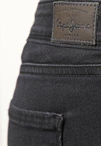 Vaqueros de denim negros con un tejido texturizado, diseño de cinco bolsillos y un parche de logo bordado con la marca "Pepe Jeans" en la parte trasera.