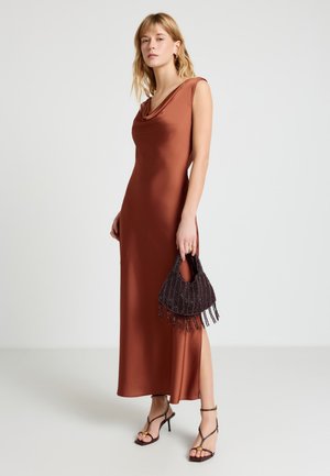 Femme portant une robe en satin couleur rouille sans manches avec une fente latérale, tenant un sac à main noir à perles et portant des talons noirs à brides.