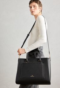 Black synthetic handbag with dual handles and a detachable shoulder strap. Features textured surface, gold hardware, and a front pocket.