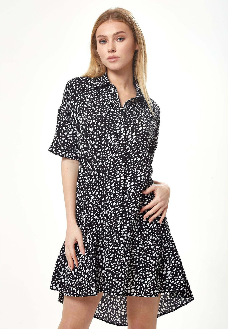 Black and white polka dot shirt dress with short sleeves, a button-up front, and a flared hemline, made of lightweight fabric.