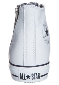 Baskets montantes en cuir blanc avec fermeture éclair, présentant un patch logo rond noir, une semelle rayée noire et une tige texturée.