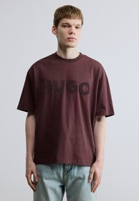 Oversize t-shirt i bordeaux lavet af bomuld med en dristig "HUGO"-logo i mørkere nuancer, korte ærmer og rund halsudskæring. Bruges sammen med denim jeans.