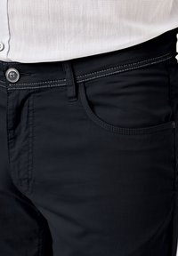 Dunkelblaue Hose aus glattem Stoff mit engem Schnitt. Verfügt über eine Vordertasche, sichtbare Nähte und einem Knopfverschluss.