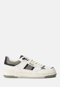 Zapatilla blanca con una suela gruesa, con acentos en gris y negro, dos franjas negras y material texturizado en el talón y la lengua.