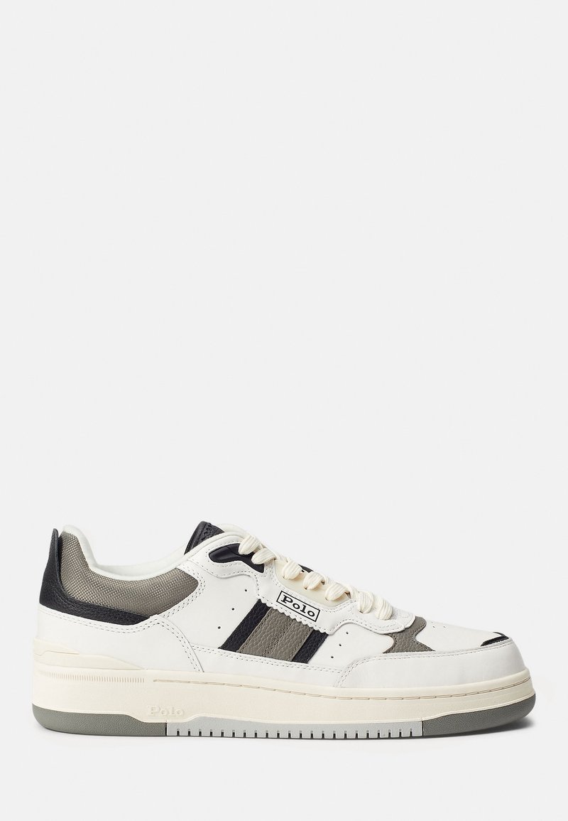 Zapatilla blanca con una suela gruesa, con acentos en gris y negro, dos franjas negras y material texturizado en el talón y la lengua.