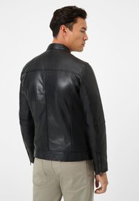 Schwarze Lederjacke mit figurschmeichelndem Design, glatter Textur und Reißverschlussmanschetten. Verfügt über einen Stehkragen und Nahtdetails auf der Rückseite.