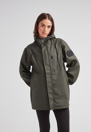 Veste à capuche imperméable de couleur vert olive foncé, dotée d'une poche zippée à l'avant, de cordons élastiques et d'un écusson rond sur la manche.