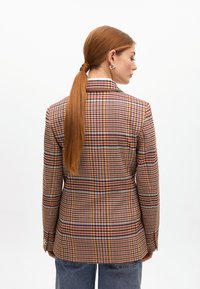 Hnedý a viacfarebný kockovaný blazer so slim fit strihom, s klopami a dlhými rukávmi, ktoré majú detaily s gombíkmi na manžetách.