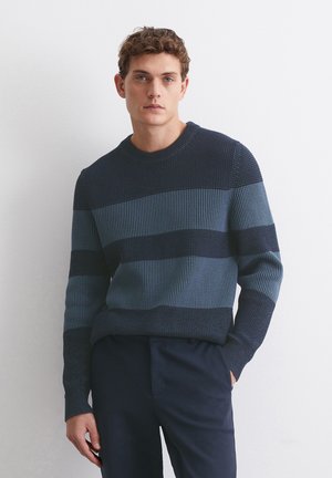Marineblauer und blauer gestreifter Pullover aus geribbeltem Strickstoff, mit Rundhalsausschnitt und langen Ärmeln, kombiniert mit dunklen Hosen.
