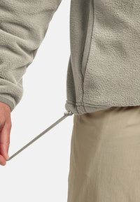 Fleece jacket in light gray with textured fabric. Features an adjustable drawstring at the hem and visible stitching accents.
