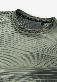 Olive green athletic shirt with black geometric pattern and round neckline, close-up showing "ACTIVE" label inside collar.