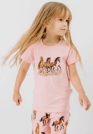 Young girl with long blonde hair wearing pink outfit featuring running horse illustrations on shirt and pants, looking to the side.